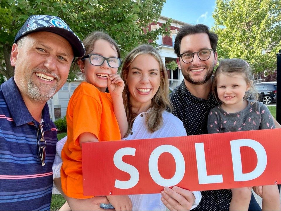 Clinton Howell Team celebrates a successful home sale with smiling clients and children holding a large red SOLD sign outdoors.