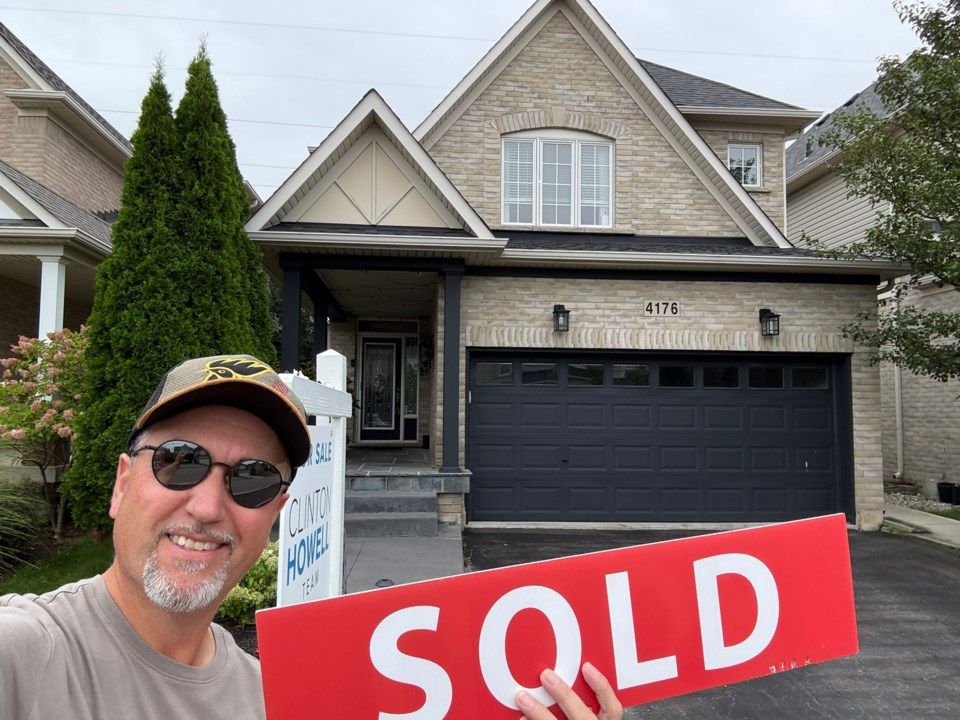 Clinton Howell smiling beside a SOLD sign outside a two-story brick home at 4176 after a successful Burlington real estate sale.
